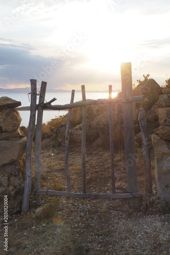 Rustic handmade wooden fence gate on a rocky hillside at sunset, scenic view of a lake and mountains in the background, peaceful rural landscape and travel destination during golden hour