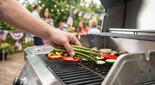 Hand placing fresh asparagus on a gas grill with other vegetables. Healthy vegetarian barbecue for a 4th of July summer party