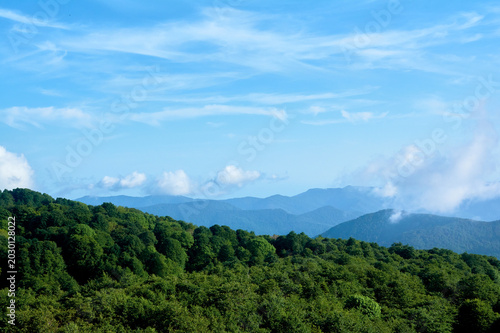 Mountains covered in dense green forest rise toward clouds, creating layered landscape where earth meets sky.
