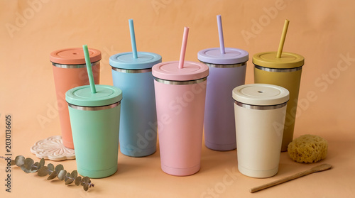 Foto Collection of insulated tumblers with straws, displayed in various matte pastel colors against a neutral background, featuring eucalyptus, a sponge, and a wooden spoon