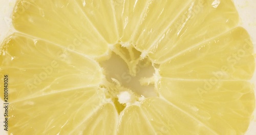 Macro top view close-up shot of a fresh round lemon slice rotating slowly. The vibrant yellow citrus fruit slice spins smoothly, showcasing its juicy pulp, detailed texture, and natural patterns