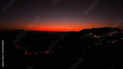 Tableau sur toile Evening sky painting red light over silhouetted mountains and twinkling town lig