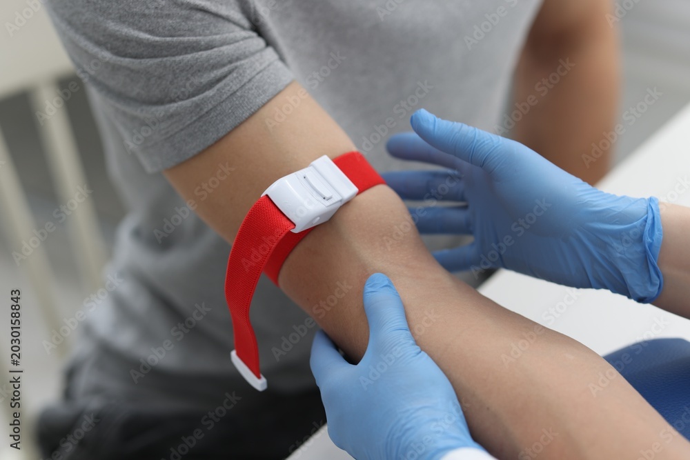 Obraz premium Nurse putting medical tourniquet on patient's arm in clinic, closeup