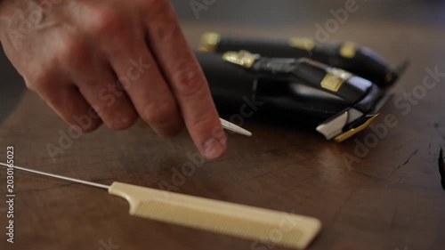 Male hairstylist's hand taking professional scissors from a wooden table with a comb and hair clipper. Hair salon workplace equipment