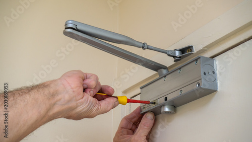 Photos Building maintenance engineer adjusting an automatic door closer on a fire door using a screwdriver