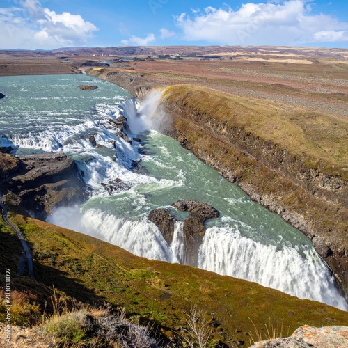 Majestic multi-tiered waterfall cascades into a rugged canyon under a bright blue sky