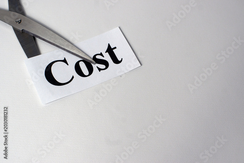 Scissors cutting the word COST on paper over a white table, representing cost reduction, budgeting efficiency, financial control, and strategic savings in business management.