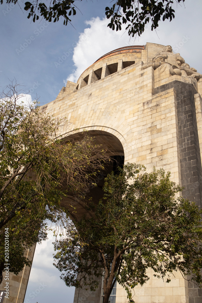 Fototapeta premium Set against a bright sky with surrounding trees, this iconic landmark in Mexico City reflects historical significance, cultural heritage, and the grandeur of large-scale urban monuments.