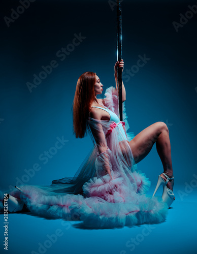 Pole dancer in a lush pink gown posing gracefully on pole in studio
