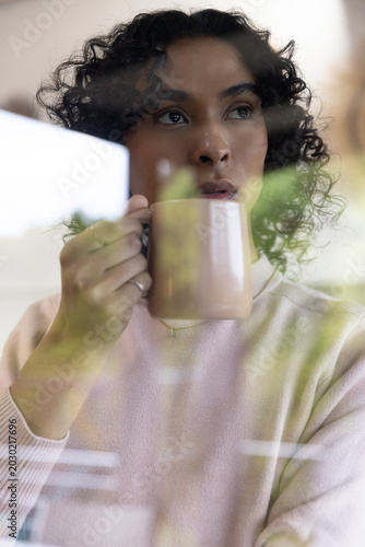 Non-binary in twenties holding pale pink mug, gazing through glass window, wearing pink sweater