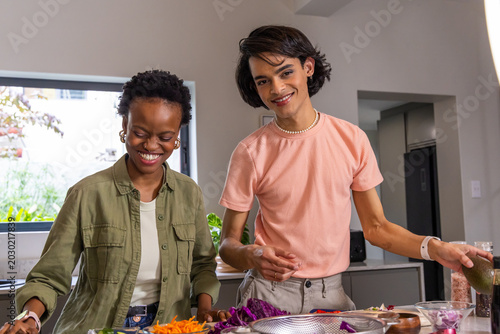 Diverse friends smiling and preparing meal at kitchen counter with shredded carrots and colander