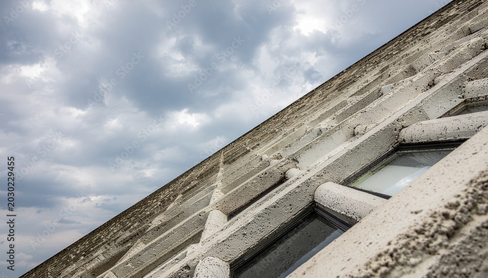 Fototapeta premium Close-up view of a modern building's textured concrete facade with integrated windows under a cloudy sky.