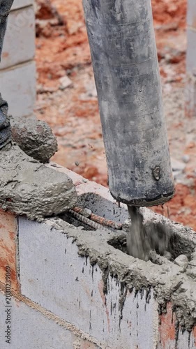 Construction worker operates concrete pump to compact fresh concrete on block wall at building site.