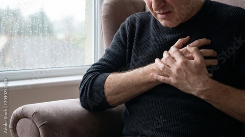 Mature man holding chest in pain suffering from a heart attack at home