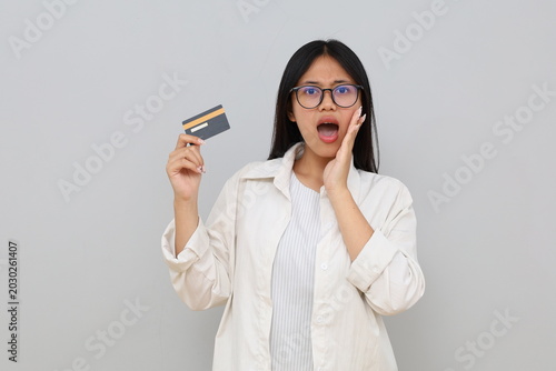 Photos Photo of an impressed young Asian woman, hand on cheek, holding debit/credit card, surprised expression, screaming happily while looking at camera, isolated on white background