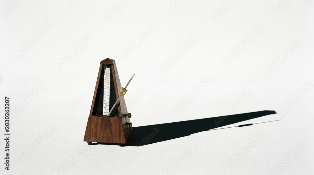 Obraz premium Clean studio composition featuring musical metronome object casting long shadow onto crisp white surface background.