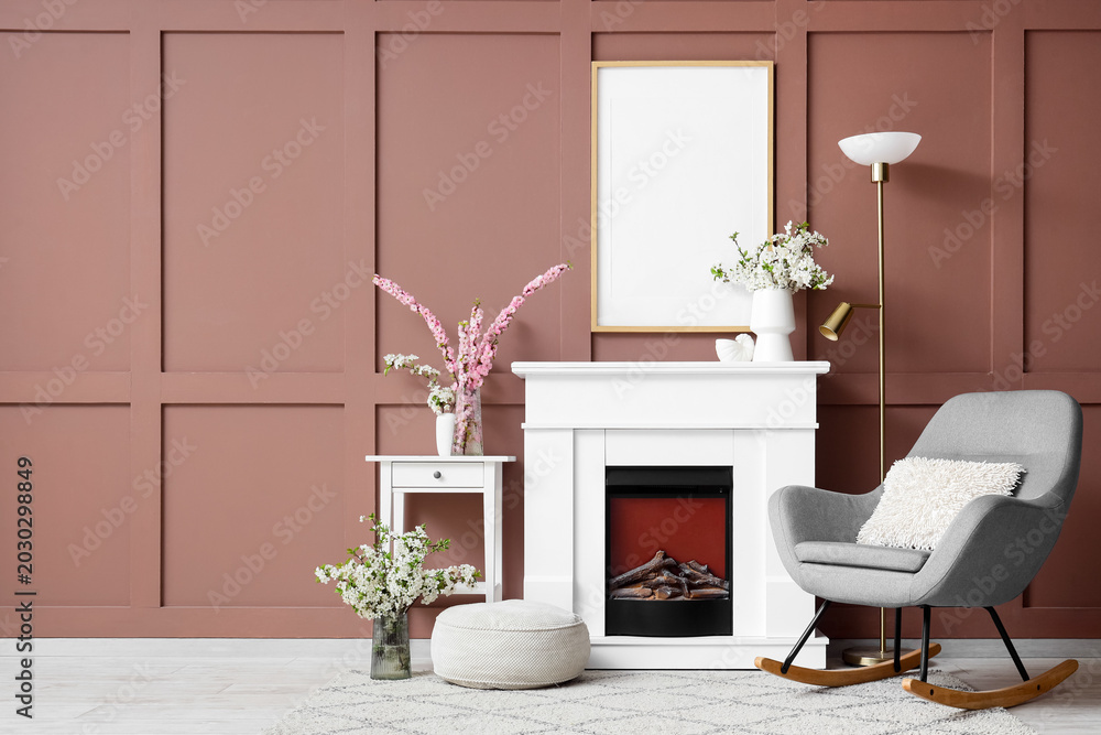 Fototapeta premium Interior of living room with blooming branches in vases, fireplace and rocking armchair