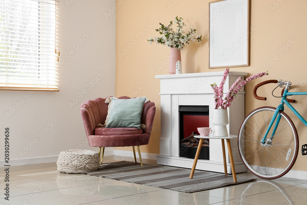 Fototapeta premium Interior of living room with fireplace, bicycle, armchair and blooming branches in vases
