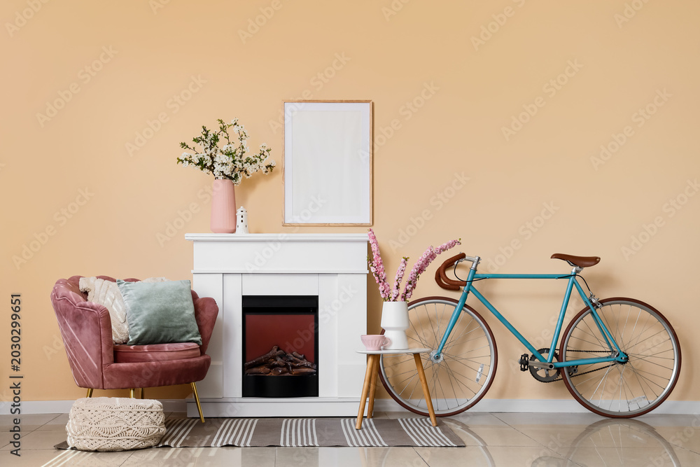 Fototapeta premium Interior of living room with fireplace, bicycle, armchair and blooming branches in vases
