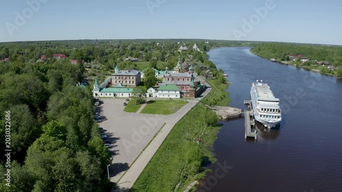 Tilt down aerial shot of cruise ship on Volkhov river nearby Nikolsky monastery on sunny summer day. Staraya Ladoga, Russia.