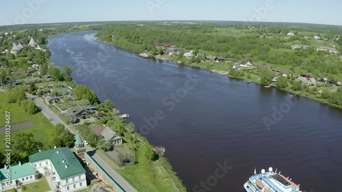 Backward reveal aerial shot of Nikolsky monastery and cruise ship on Volkhov river on sunny summer day. Staraya Ladoga, Russia.