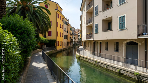 Canal runs through buildings with palm trees and walkway on a sunny day