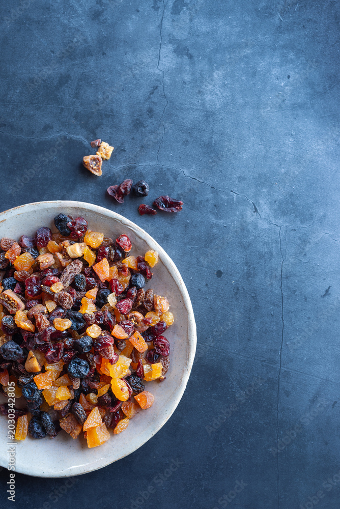 Fototapeta premium Mixed dried fruits in a ceramic bowl on a dark background.