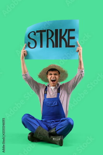 Protesting male farmer holding placard with word STRIKE on green background