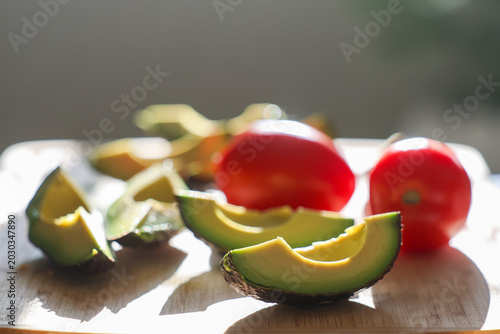 Fresh green avocado sliced and ready to eat along with whole organic roma tomatoes on a cutting board. Delicious healthy, nutritious food.