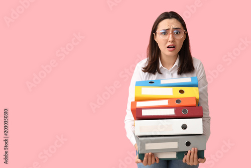 Foto Stressed young businesswoman with document folders on pink background