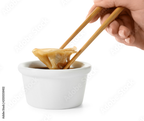 Woman dipping tasty Chinese jiaozi into sauce on white background