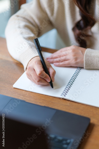 Foto Vertical closeup image of a woman writing on a notebook while working on laptop