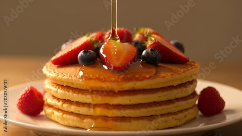 Pancakes with strawberries and syrup being poured.