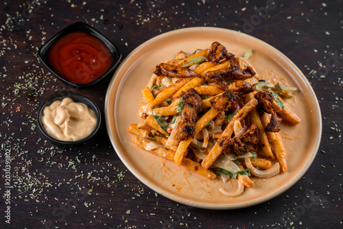 Foto A plate of loaded fries with meat and toppings served with dipping sauces on a table