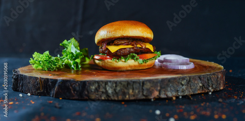 A juicy burger with cheese lettuce tomato and onion on a wooden board