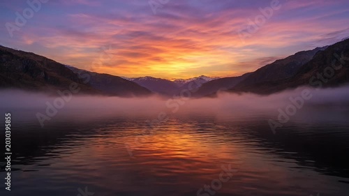 Sunset over foggy lake and mountains.