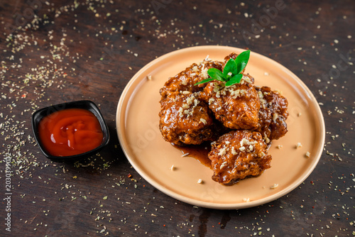 Quadro em tela A plate of spicy fried chicken wings with herbs on a wooden table next to a small bowl of sauce
