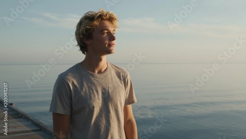 Young man looking out at calm sea from wooden dock