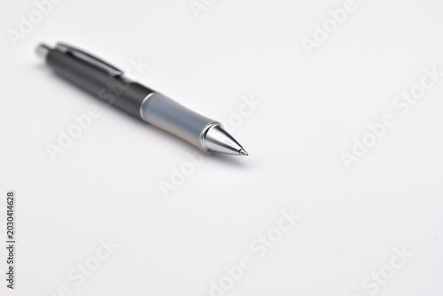 A sleek black and silver ballpoint pen rests on white paper, invoking writing, office work and business planning. Soft shallow focus highlights the pen tip and clean minimal stationery aesthetic.
