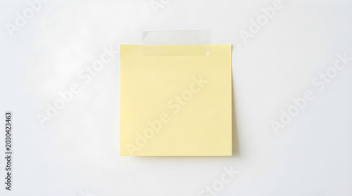 Blank yellow square sticky note taped to a clean white wall surface with cut out self adhesive reminder stationery copy space minimalist studio shot isolated essential creativity planning