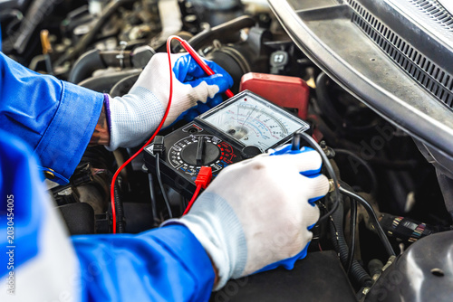 An automotive technician using multimeter to diagnose the electrical system in auto repair shop