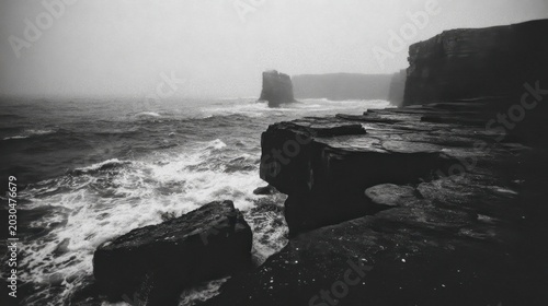 Thick damp fog hugs a rugged coastline with crashing waves against dark rocky cliffs