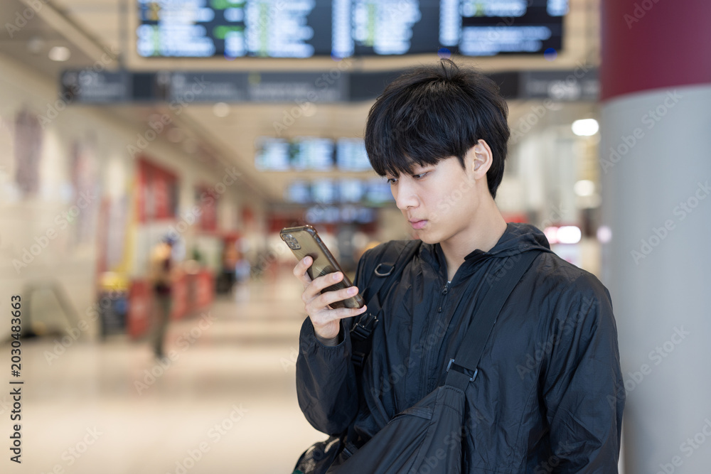Fototapeta premium Young Man Using Smartphone at Bus Terminal Waiting Area