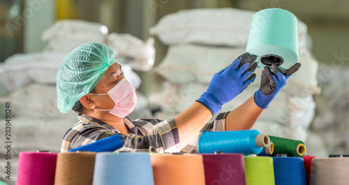 Tableau sur toile Textile factory male worker in mask hairnet and gloves handling and checking col