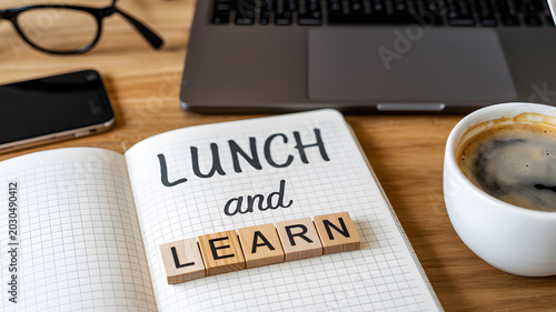 A notebook with lunch and learn written on it surrounded by office supplies on a wooden desk