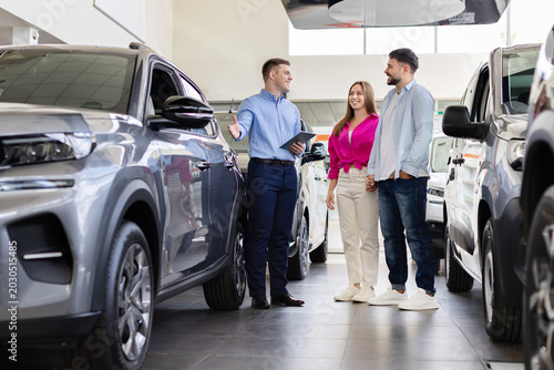 Fotografía Young couple choosing a new vehicle at modern car dealership showroom while prof