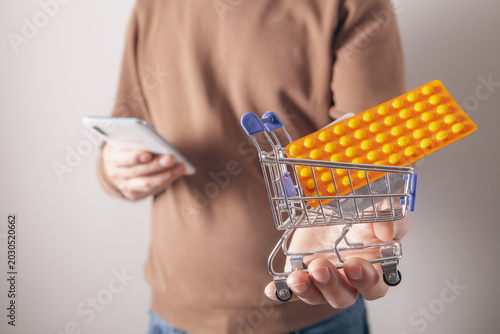 Woman holding a shopping cart with pills and a smartphone in her hand