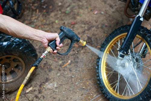 Focused hand performs maintenance, washing muddy motorcycle wheel. powerful high pressure washer spray and water jet provide deep cleaning for dirty bike part on ground