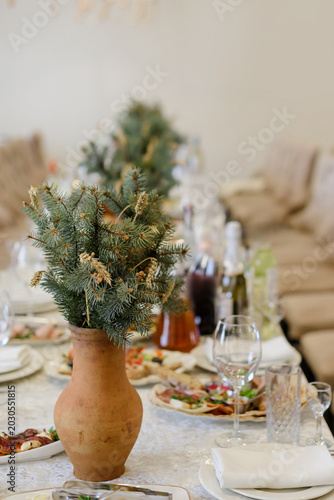A festive table setting at a banquet featuring a traditional clay vase filled with spruce branches and wheat ears as a rustic centerpiece decoration.