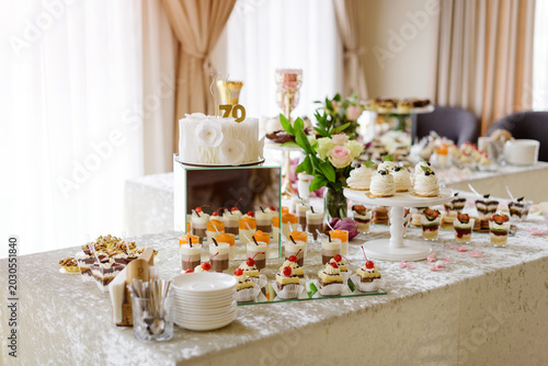 A lavishly decorated dessert table candy bar at a luxury event featuring pavlova cakes, verrines, pastries, and a birthday cake.